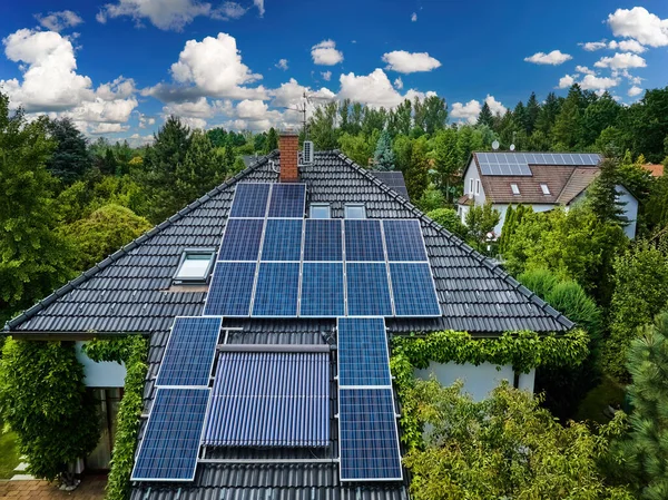 Aerial view of the roofs of houses covered with solar panels. Family houses in gardens, photovoltaic panels on the roof, summer, blue sky with white clouds. Home Electricity Generation, green living.