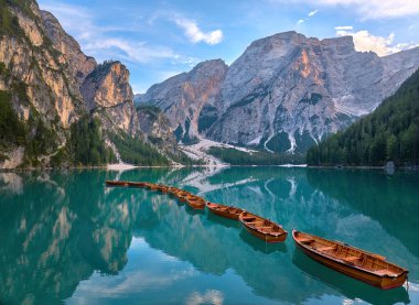 Dolomitlerdeki Pragser Wildsee, Lago di Braies 'in panoramik fotoğrafı. Dağın tepesindeki ahşap teknelerin arasından yeşil-mavi göl manzarası ve batan güneş.