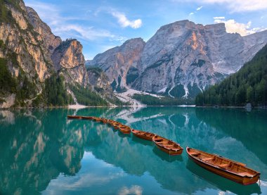 Panoramic photo of Lago di Braies, Pragser Wildsee in the Dolomites. View of the whole green-blue lake through wooden boats on the mountain peak and the setting sun. clipart