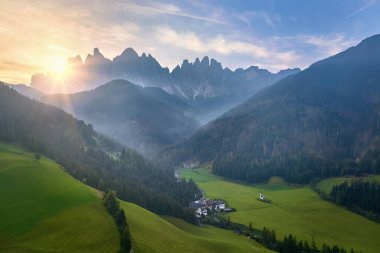 Seyahat eden Dolomitler teması: Güney Tyrol 'daki Dolomitlerin sabah manzarası, İtalyan Alpleri. Santa Magdalena 'nın beyaz kilisesinin hava manzarası, yeşil çayırlar ve dik kayalıklar..
