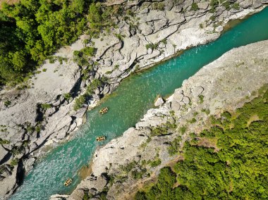 Beyaz su raftingi. Macera ve spor. Sarı bir sal kristal berraklığında kayaların arasında süzülüyor, mavi-yeşil su. Arnavutluk 'un Vjose Nehri üzerinde yüzen kirişlerin dikey drone görüntüsü.