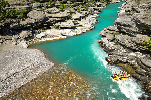 White water rafting.  Adventure and sport. A yellow raft floating among the rocks on the crystal clear, blue-green water. Perpendicular drone view of the rafters floating on Vjose river, Albania.
