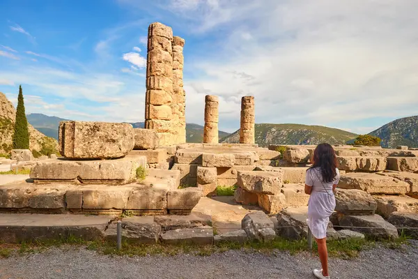 一个长头发的女人从后面看着阿波罗神殿或阿波罗 以及日落时的背脊柱子 旅游胜地 以阿波罗圣地的神谕闻名 希腊德尔菲Parnassus山 图库图片