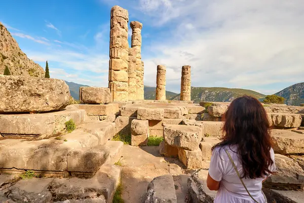 一个长头发的女人从后面看着阿波罗神殿或阿波罗 以及日落时的背脊柱子 旅游胜地 以阿波罗圣地的神谕闻名 希腊德尔菲Parnassus山 免版税图库照片