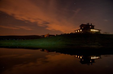 Mountain hut at night reflecting in the lake