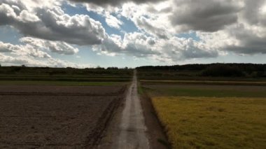 Mavi günde, kara bulutların altında kuru tarlaların arasından toprak yolu daralt. Yüksek kalite 4k görüntü