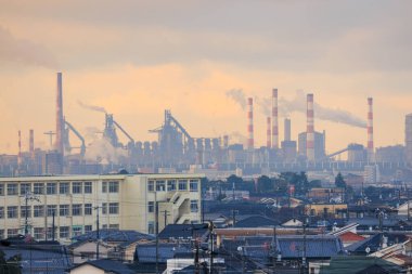 Gökyüzündeki günbatımı rengi küçük kasabalardaki evlerden endüstriyel baca bacalarına kadar uzanıyor. Yüksek kalite fotoğraf