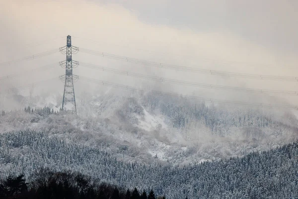 stock image High voltage electrical transmission tower and wires over snowy mountain landscape. High quality photo