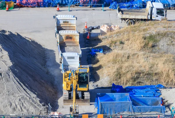 Earth mover and flatbed trucks parked by sand piles at empty construction site on sunny day. High quality photo