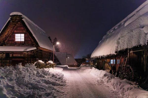 Snow piles along cleared road by traditional wooden houses in village at night. High quality photo
