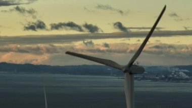 Spinning Wind Turbine with Distant Emission from Industrial Plant at Sunset. High quality 4k footage
