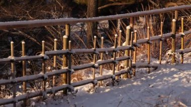 Slow pan over traditional Japanese bamboo fence in snow at golden hour. High quality 4k footage
