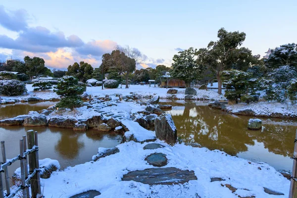 Dawn in Japanese garden with stone path and bridge through snow over pond . High quality photo