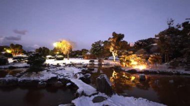 Snow covered stone bridge over pond in illuminated Japanese garden at dawn. High quality 4k footage
