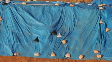 Wind blows blue tarp weighted down by sandbags protecting outdoor materials. High quality 4k footage