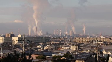 Smoke billows from chimneys at industrial plant by residential neighborhood. High quality 4k footage