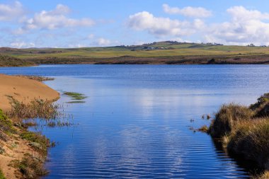 Sahildeki lagünün sakin mavi suları ve arka planda yuvarlanan yeşil tepeler. Yüksek kalite fotoğraf