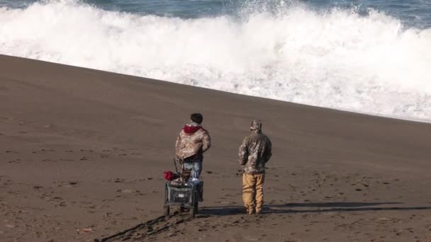 Двоє Рибалок Вітряний День Дивляться Хвилі Розбиваються Берег Піщаного Пляжу — стокове відео