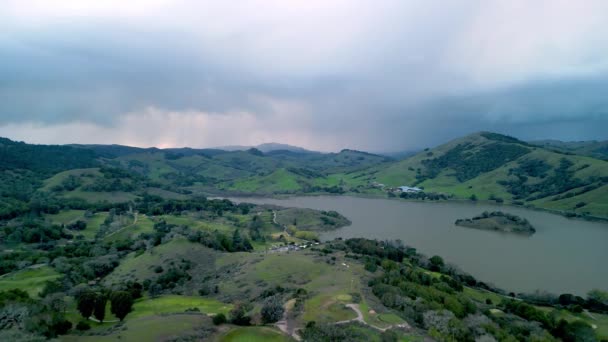 緑のカリフォルニアの丘で穏やかな湖に近づいて嵐の空中ビュー 高品質4K映像 — ストック動画
