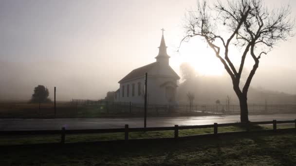 霧と霧の中で輝く明るい朝の太陽と小さな田舎のアメリカの教会 高品質4K映像 — ストック動画