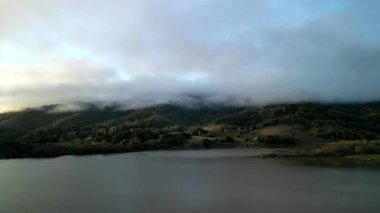 Sabaha karşı sislerle kaplı dağlarla gölgeli suların üzerinde alçaktan uçmak. Yüksek kalite 4k görüntü
