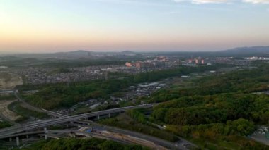 Güneş panellerini gökyüzünde günbatımı renginde göstermek için şehrin sınırındaki otobanda uçmak. Yüksek kalite 4k görüntü