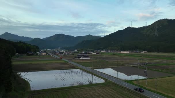 黄昏时分 汽车在乡村路上沿着稻田开到山脚下的村庄 高质量的4K镜头 — 图库视频影像