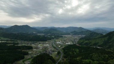 Dağ zirveleriyle vadideki küçük bir kasabaya giden otoyolun havadan görünüşü. Yüksek kalite 4k görüntü