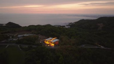 Gün batımında sessiz adadaki karanlık ağaçlardaki parlak restoranın hava manzarası. Yüksek kalite 4k görüntü