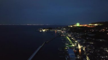 Gece karanlik sahil kasabasindan gecen yolda arabalarin isiklari yaniyor. Dönme dolaba uzaklik konuyor. Yüksek kalite 4k görüntü