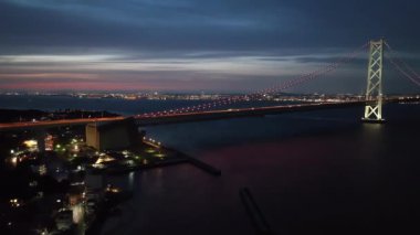 Geceleyin asma köprüde hafif trafik ve gökyüzünde gün batımı parıltısı. Yüksek kalite 4k görüntü