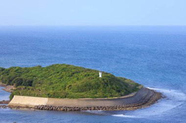 Beton deniz duvarı, deniz feneri olan küçük yeşil adada kıyı şeridini korur. Yüksek kalite fotoğraf