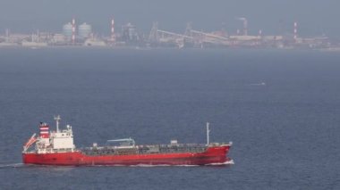 Osaka, Japonya - 23 Mayıs 2023: Küçük kırmızı kargo gemisi kıyıdaki sanayi tesislerinde bacalardan geçiyor. Yüksek kalite 4k görüntü
