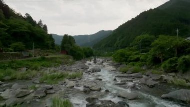 Yeşil dağ manzarasında kayalık nehrin üzerinde alçaktan uçuyor. Yüksek kalite 4k görüntü