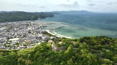 Awaji kıyısındaki Sumoto yakınlarında eski bir şatoyla ormanlık tepenin üzerinde uçuyor. Yüksek kalite 4k görüntü