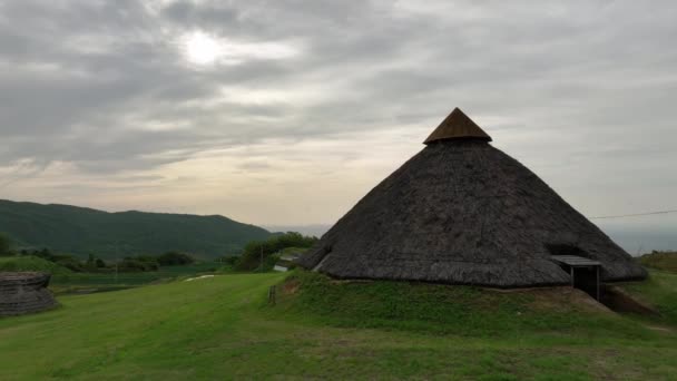 草の丘の上にある縄文時代の茅葺き屋根の小屋を中心に回っています 高品質4K映像 — ストック動画