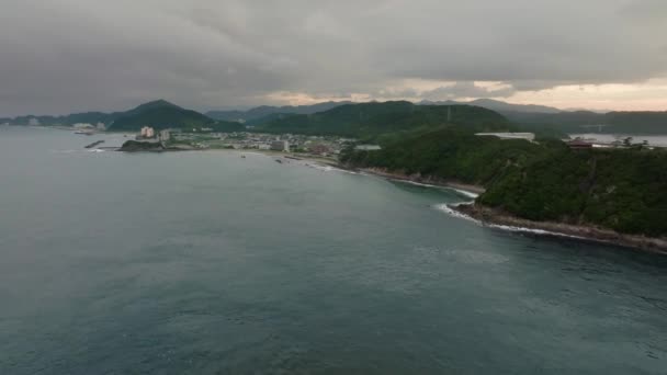 日没時に緑の山々によって沿岸の町に穏やかな青い海の上を飛んでいます 高品質4K映像 — ストック動画