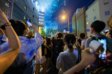 Kalabalık sokakta telefonla fotoğraf çekerken havai fişekler gökyüzünü aydınlatıyor. Yüksek kalite fotoğraf