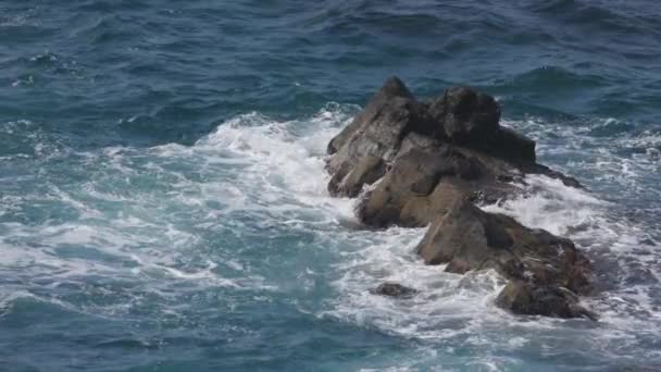 阳光明媚的日子里 海浪在靠近海岸的蓝色海洋的岩石上喷溅 高质量的4K镜头 — 图库视频影像