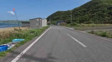 Güneşli bir günde Rebun Adası sahil yolunda evlerin ve barakaların önünden geçmek. Yüksek kalite 4k görüntü