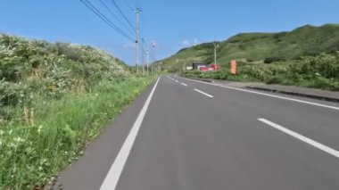 Güneşli bir yaz gününde Rebun Adası 'ndaki çimenli tepelerin ve evlerin yanından geçiyoruz. Yüksek kalite 4k görüntü