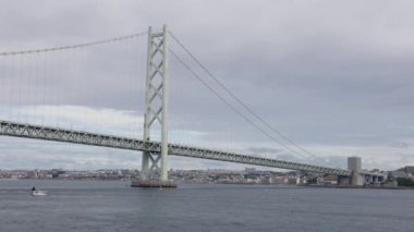Akashikaikyo köprü kuleleri üzerlerinde bulutlar olan sakin sularda küçük bir teknenin üzerinde. Yüksek kalite 4k görüntü