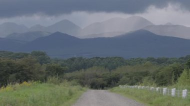 Japonya, Hokkaido 'da yağmur bulutlarının altında yeşil kırsal bölgelerden dağlara uzanan kirli bir yol. Yüksek kalite 4k görüntü