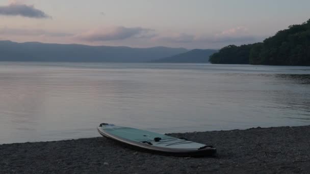 シングルスタンドアップパドルボードは 日没時に山の落ち着いた湖でビーチで 高品質の4K映像 — ストック動画