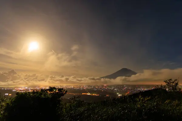 Bright full moon lights clouds over city at base of Mt. Fuji at night. High quality photo