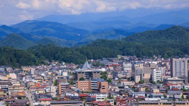 Takayama, Japan - August 4, 2024: Elevated view of dense buildings in Takayama city by green mountains on sunny day. High quality photo clipart