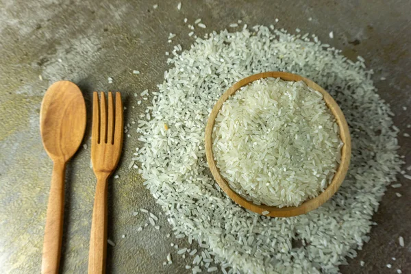 raw rice in wooden bowl with wooden spoon and fork. dry rice or uncooked rice.