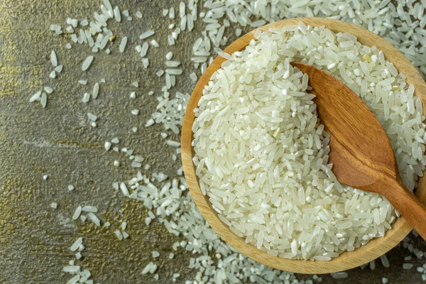 raw rice in wooden bowl with wooden spoon and fork. dry rice or uncooked rice.