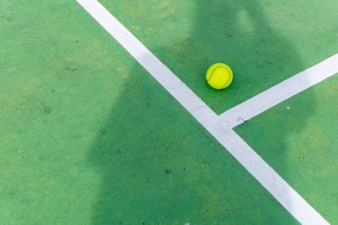 Yeşil kortta sarı tenis topu ve beyaz çizgiler. Güneşli günde kortta tenis oyuncusu gölgesi