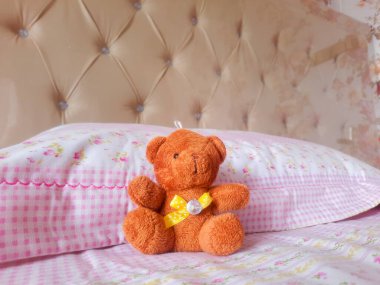 Yatak odasındaki pembe yatakta tek başına oturan sevimli ayı bebeği. Küçük oyuncak ayı çocuk odasında oynamak için kullanılıyor.